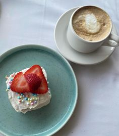 a piece of cake on a plate next to a cup of cappuccino