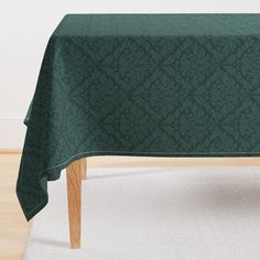 a table with a green tablecloth on it in front of a white rug and wall