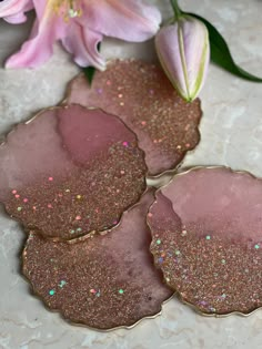 three pink and gold coasters sitting on top of a table next to a flower