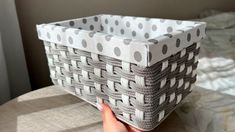 a hand holding a basket on top of a bed with white and gray polka dots