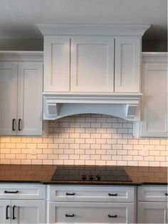 a kitchen with white cabinets, black counter tops and an oven hood over the stove