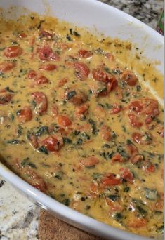 a casserole dish with tomatoes and spinach in it on a granite counter