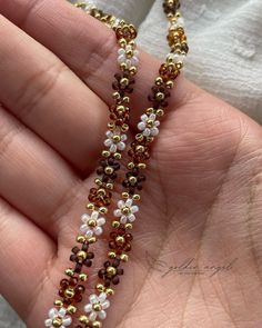 a hand holding a beaded necklace with gold and white beads hanging from it's side