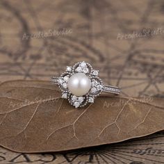 a white pearl and diamond ring sitting on top of a leaf shaped piece of paper