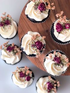 cupcakes with white frosting and purple flowers on top are arranged on a wooden platter