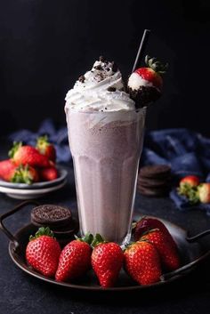 a chocolate milkshake with whipped cream and strawberries on a plate next to cookies