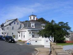 a large white house with a steeple on the top and two cars parked in front