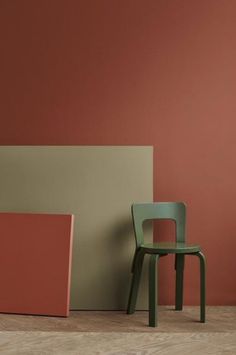 an empty chair next to a red and green box on the floor in front of a pink wall