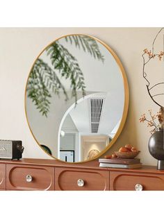 a round mirror sitting on top of a dresser next to a vase and plant in front of it