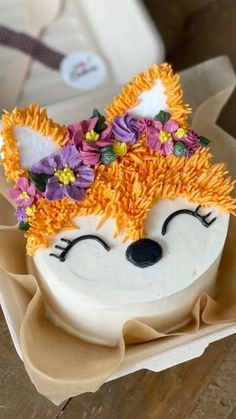 a cake decorated like a fox with flowers in its hair is sitting on a cardboard box