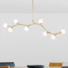 a modern chandelier hangs over a dining room table with chairs and a bowl on it