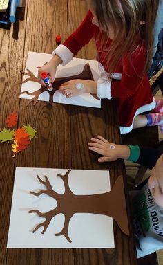 two children are making paper cutouts with the tree on them and one child is holding a crayon