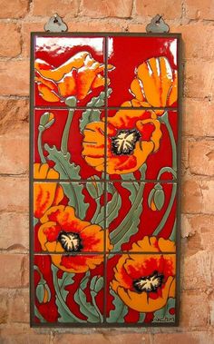 a red and yellow tile with flowers on it's side is mounted to a brick wall