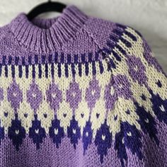 a purple and white knitted sweater hanging on a wall