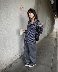 a woman standing next to a wall holding a cup and pointing at something in her hand