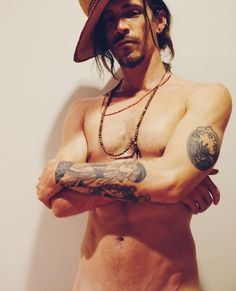 a shirtless man wearing a cowboy hat and holding his arms crossed with both hands