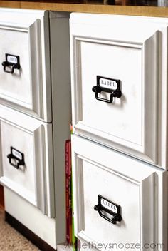 two white filing cabinets with black handles on each drawer and books in the back ground