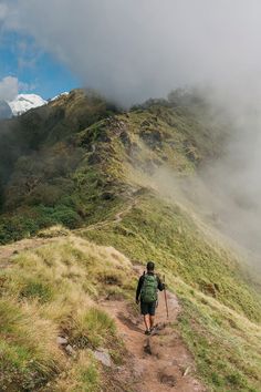 a man hiking up the side of a lush green mountain covered in fog and clouds