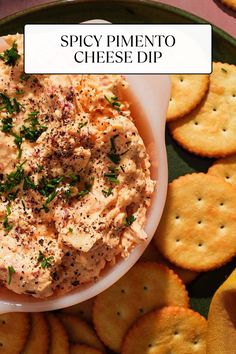 a bowl of dip surrounded by crackers on a plate with the words spicy pimentoo cheese dip