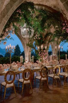 an outdoor dining area with chandeliers and flowers on the table, surrounded by greenery