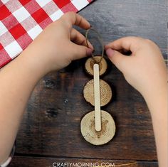 two hands are working on an object made out of wood and rope, with a red checkered table cloth in the background