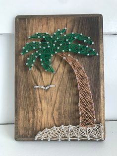 a string art palm tree on a wooden plaque with white and green beads hanging from it's sides