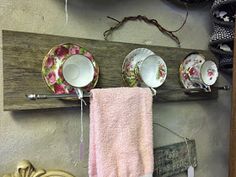 teacups and saucers are hanging on a wooden rack next to a pink towel