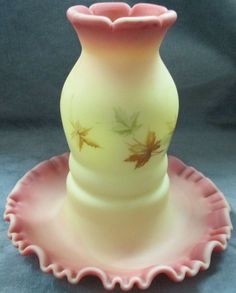 a yellow and pink glass vase sitting on top of a pink saucer with leaves painted on it