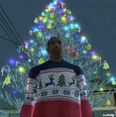 a man standing in front of a christmas tree with lights all around him and his sweater on