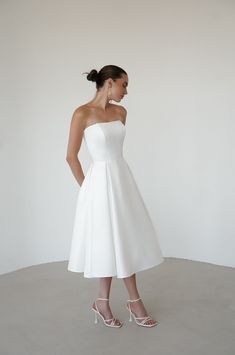 Elevate your wedding day look with our exquisite satin minimalist wedding dress. This sophisticated dress features a graceful midi length, perfect for the modern bride seeking timeless elegance. Discreet side pockets add a practical and stylish touch. A romantic lace-up back detail offers a customizable fit and a hint of classic charm. Crafted from luxurious satin, this dress combines simplicity with refined beauty, making it an ideal choice for your special day. Simple Civil Wedding Dress Courts, Simple Wedding Dress Midi, Midi Wedding Dress Tea Length, White Dresses Classy, Minimalistic Wedding Dress, Reception Dress Wedding, Simple Classy Wedding Dress, Wedding Dress Midi, White Dress Midi