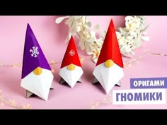 three paper gnomes sitting next to each other on a pink surface with snowflakes in the background