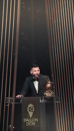 a man in a tuxedo standing at a podium with a ballon d'or trophy