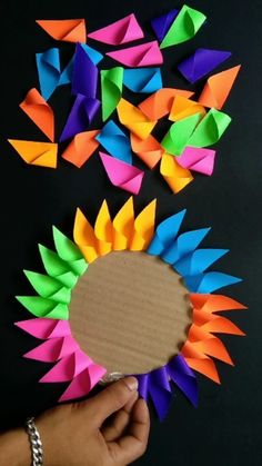 someone is holding a paper plate with colorful origami pieces around it on a black surface