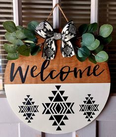 a welcome sign hanging from the side of a door with greenery and bows on it