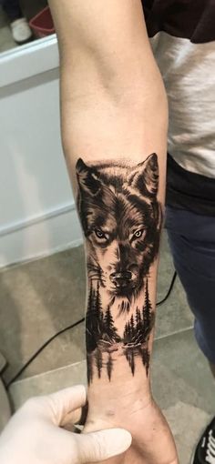 a person with a tattoo on their arm holding up a small wolf in the woods