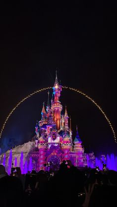 the disneyland castle is lit up at night with purple and blue lights on it's side