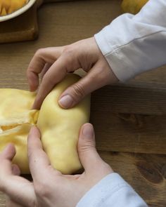 two hands are peeling cheese on a wooden table