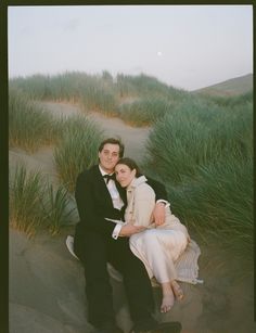 a man and woman sitting next to each other on a bench in the sand dunes