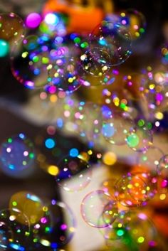 many bubbles are floating in the air with colored lights behind them and blurry background