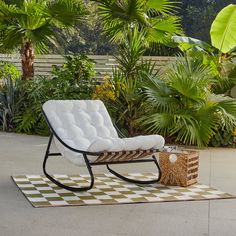 a white chair sitting on top of a checkered rug in front of palm trees