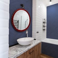 a bathroom with blue walls and marble counter top, white bathtub and round mirror