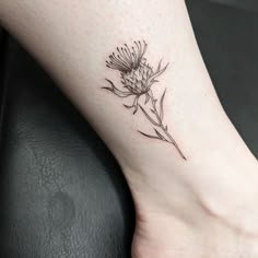 a small flower tattoo on the ankle is shown in black and grey ink, while it's still attached to a woman's leg