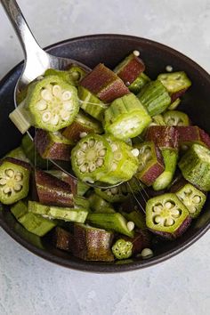 a bowl filled with green and red vegetables next to a spoon on top of a table