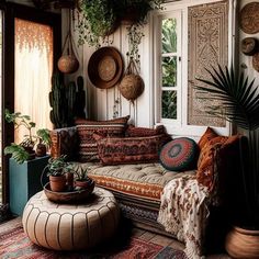 a living room filled with lots of plants and pillows on top of a rug next to a window