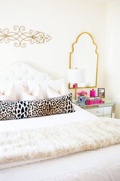 a white bed topped with pillows next to a mirror