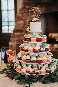 a tiered cake with cupcakes and greenery on the table