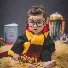 a little boy wearing glasses and a harry potter scarf sits on the floor with his wand