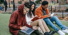 three young people sitting on the grass with laptops and books in their lap tops