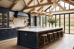 a large kitchen with blue cabinets and marble counter tops, gold pendant lights hanging from the ceiling