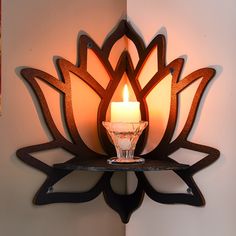 a lit candle sitting on top of a wooden shelf next to a wall mounted art piece